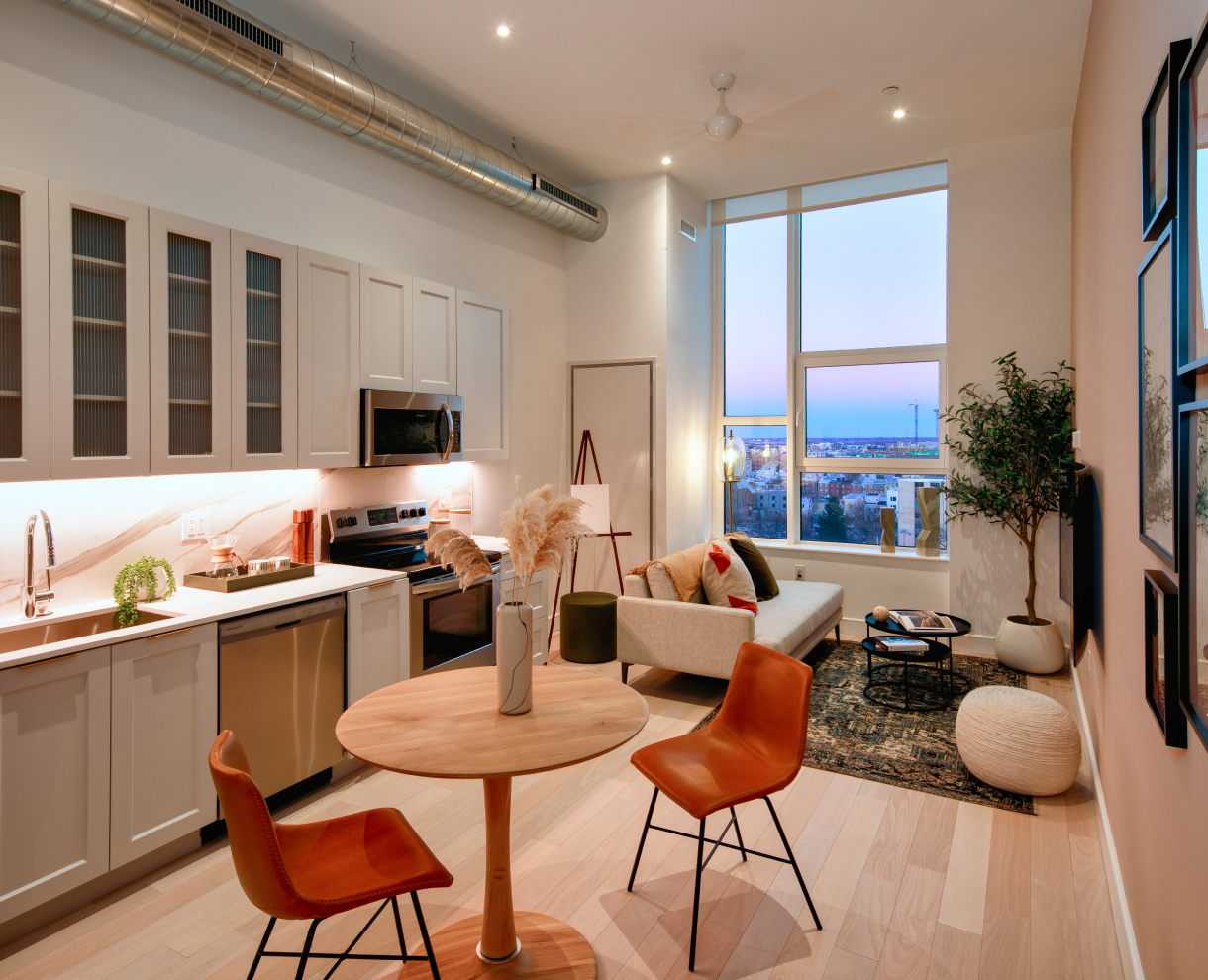 Apartment interior with kitchen and living room area including sofa, red dining chairs, and sink