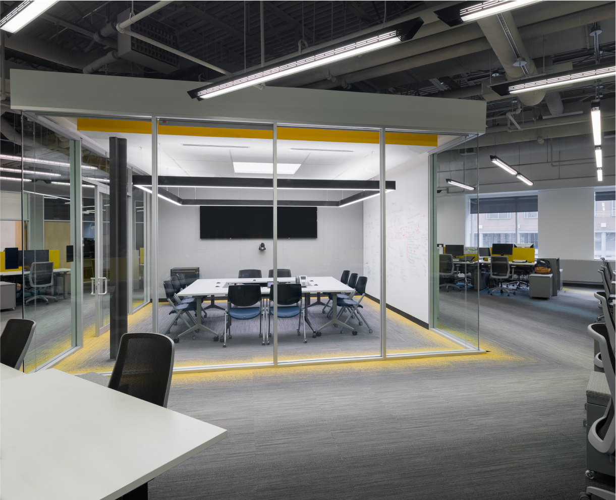 Office cube with a big desk, a lot of chairs around it, and a big screen on the wall