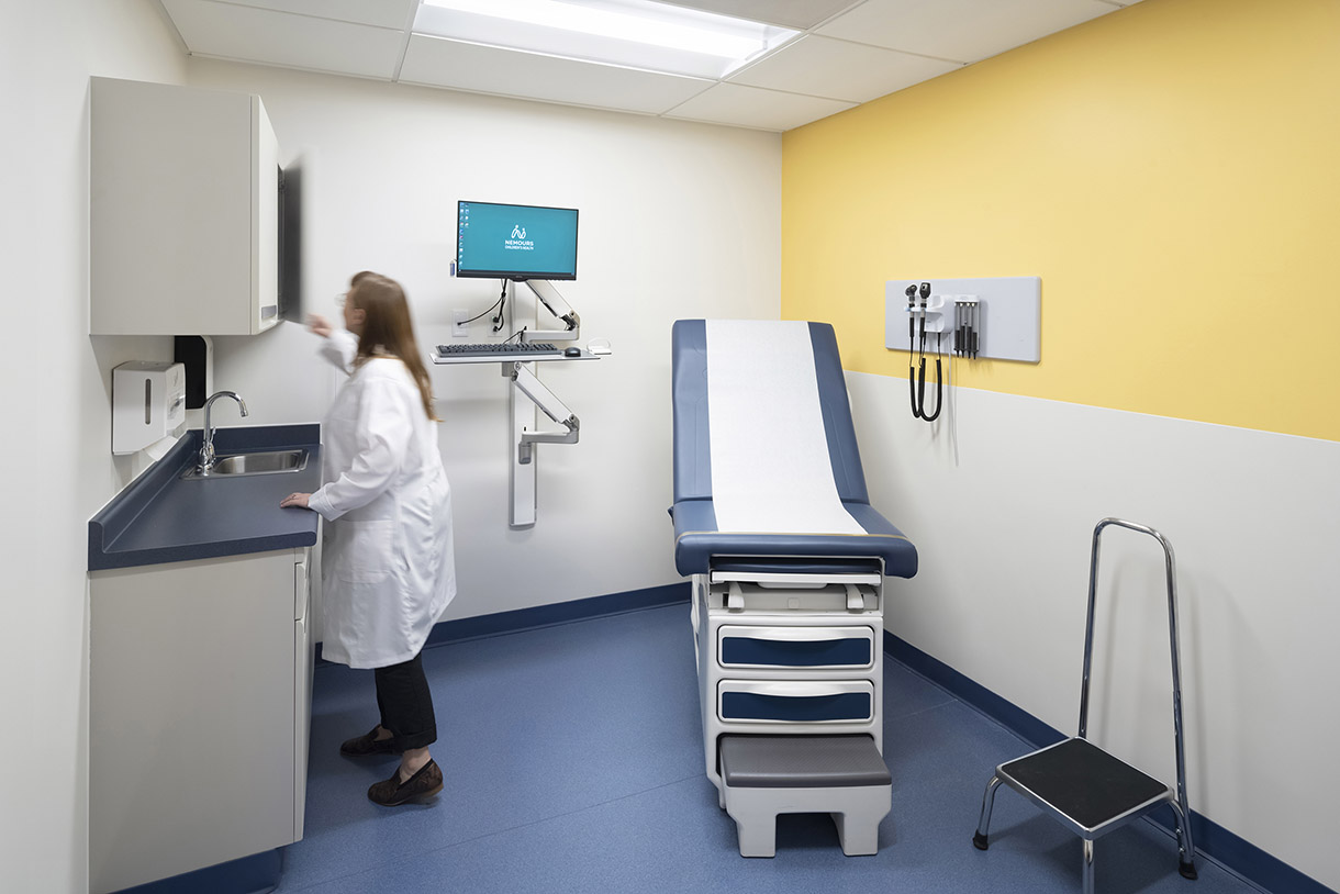 a photo of an exam room, a nurse reaches into a cabinet