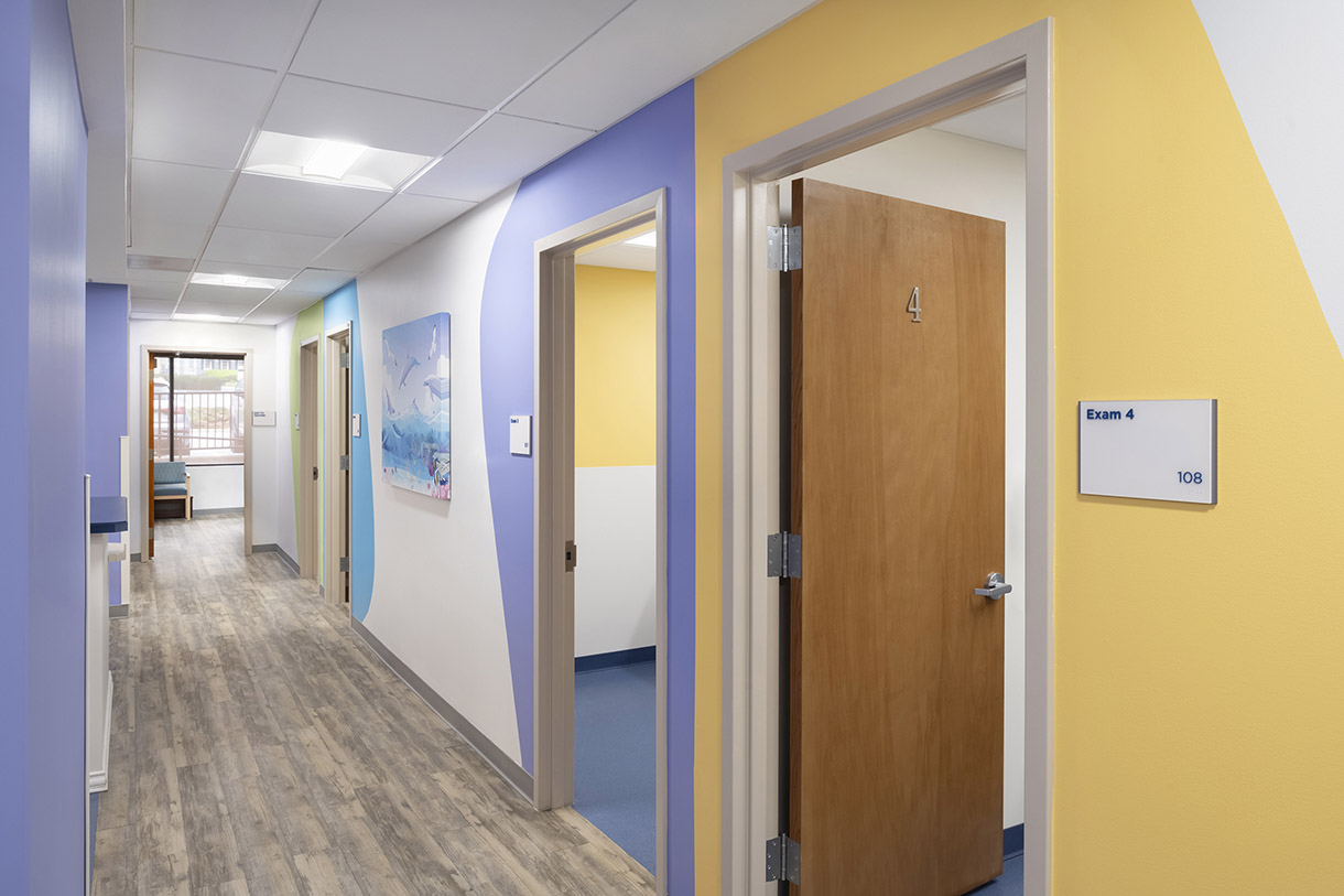 a hallway showing the entrances to exam rooms. the walls are painted a different color around each exam room door as a way to assist with navigation and appear more playful