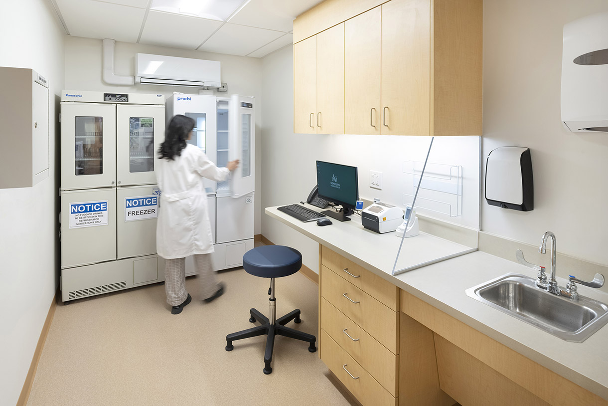 a photo of a medicine room. a nurse reaches into a freezer to retrieve some medicine