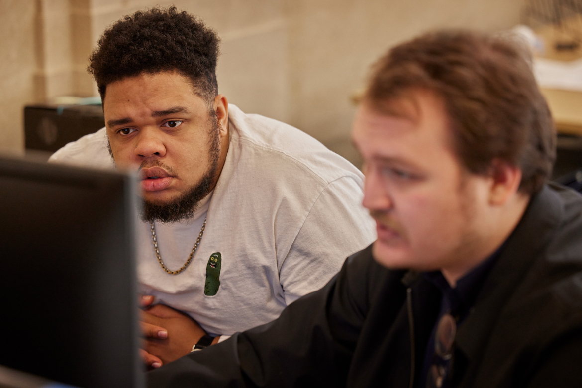 Two men are looking at a monitor, with a man in front slightly blurred in the foreground