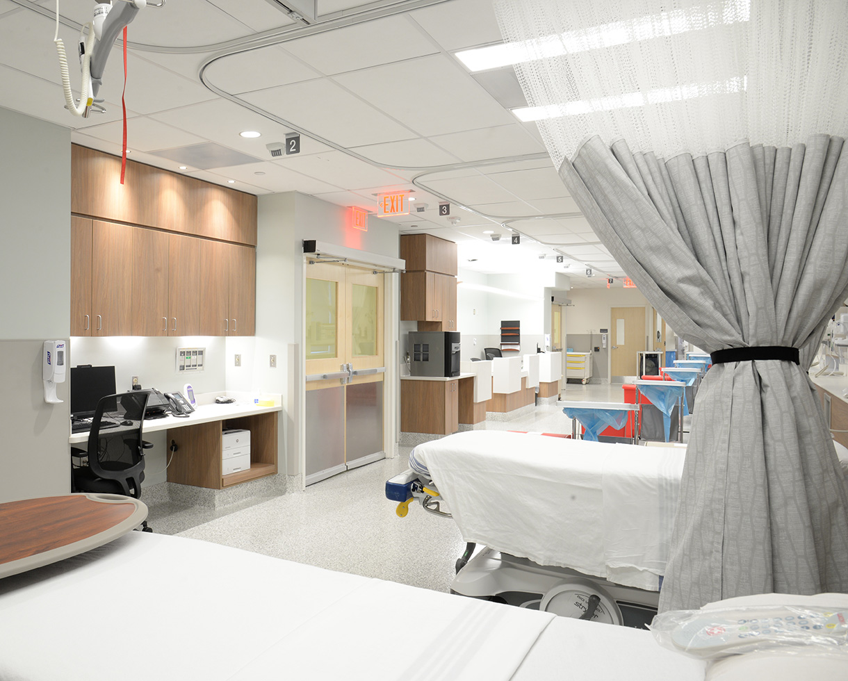 a row of beds and dialysis machines, separated by privacy curtains